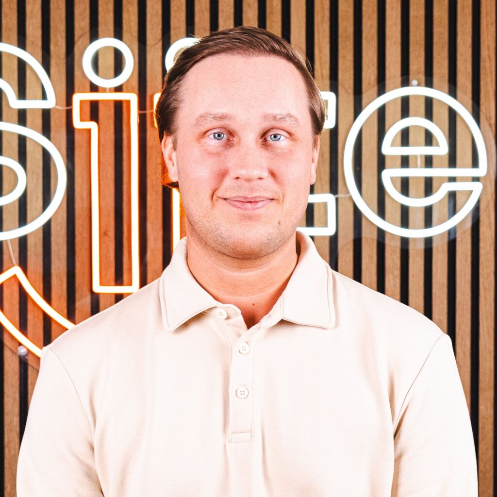 Mand smiler foran lysende firmalogo på trævæg