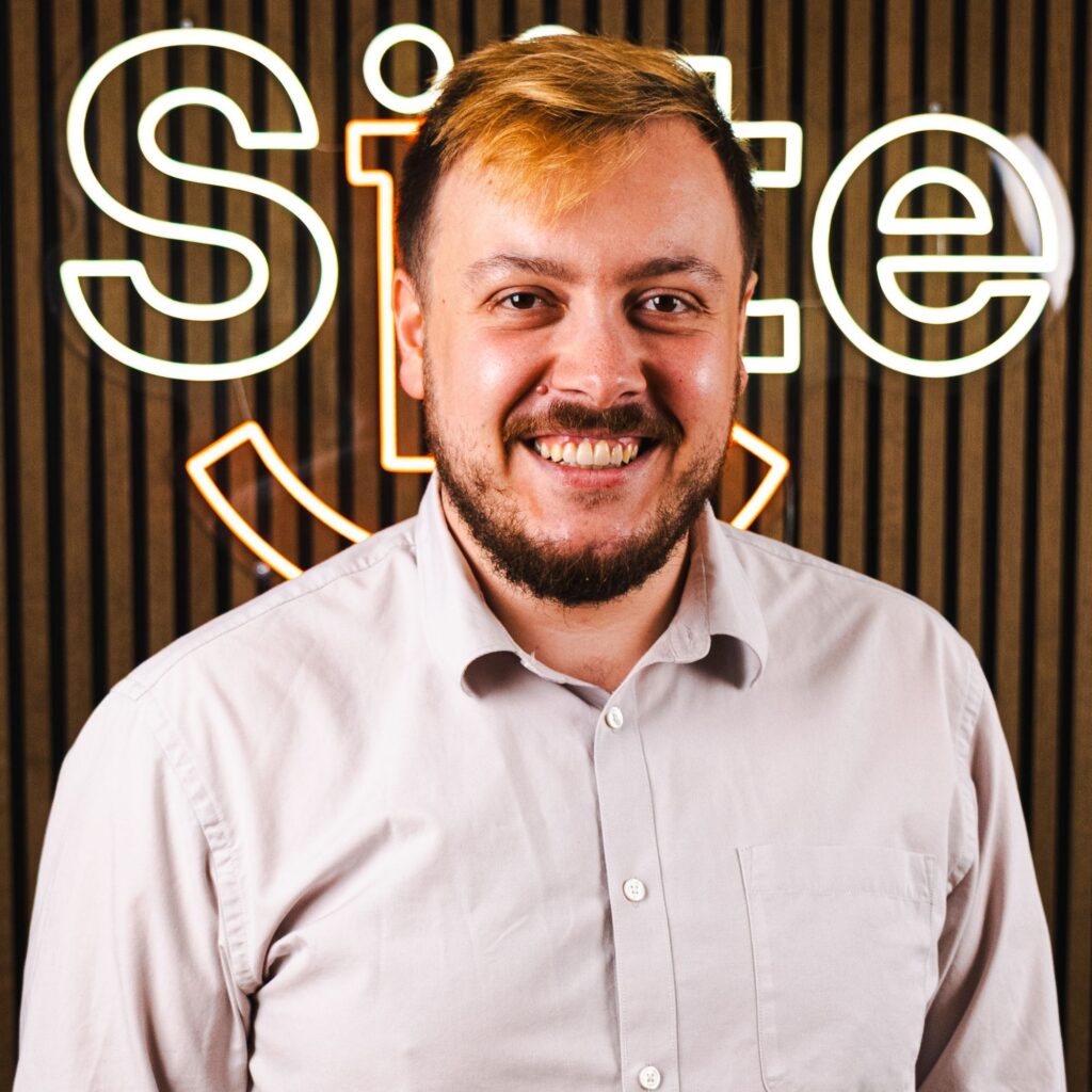 Smilende mand foran neon skilt