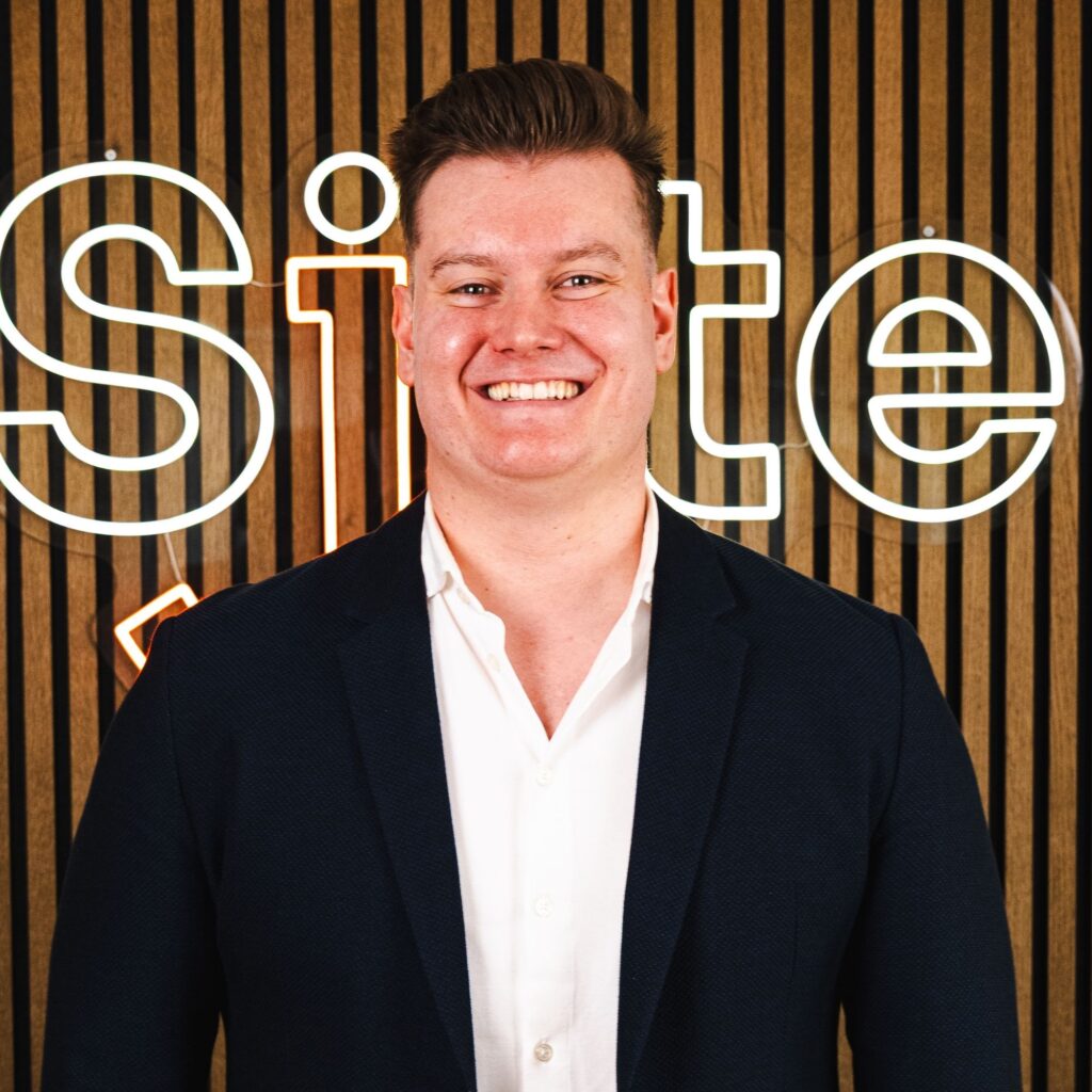 Smilende mand foran stribet baggrund og neonskilt.