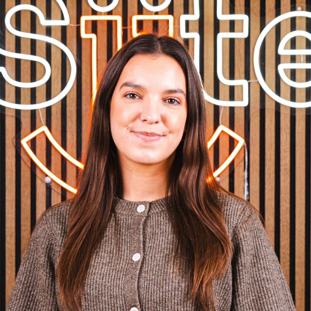 Kvinde smiler foran neonskilt med træbaggrund