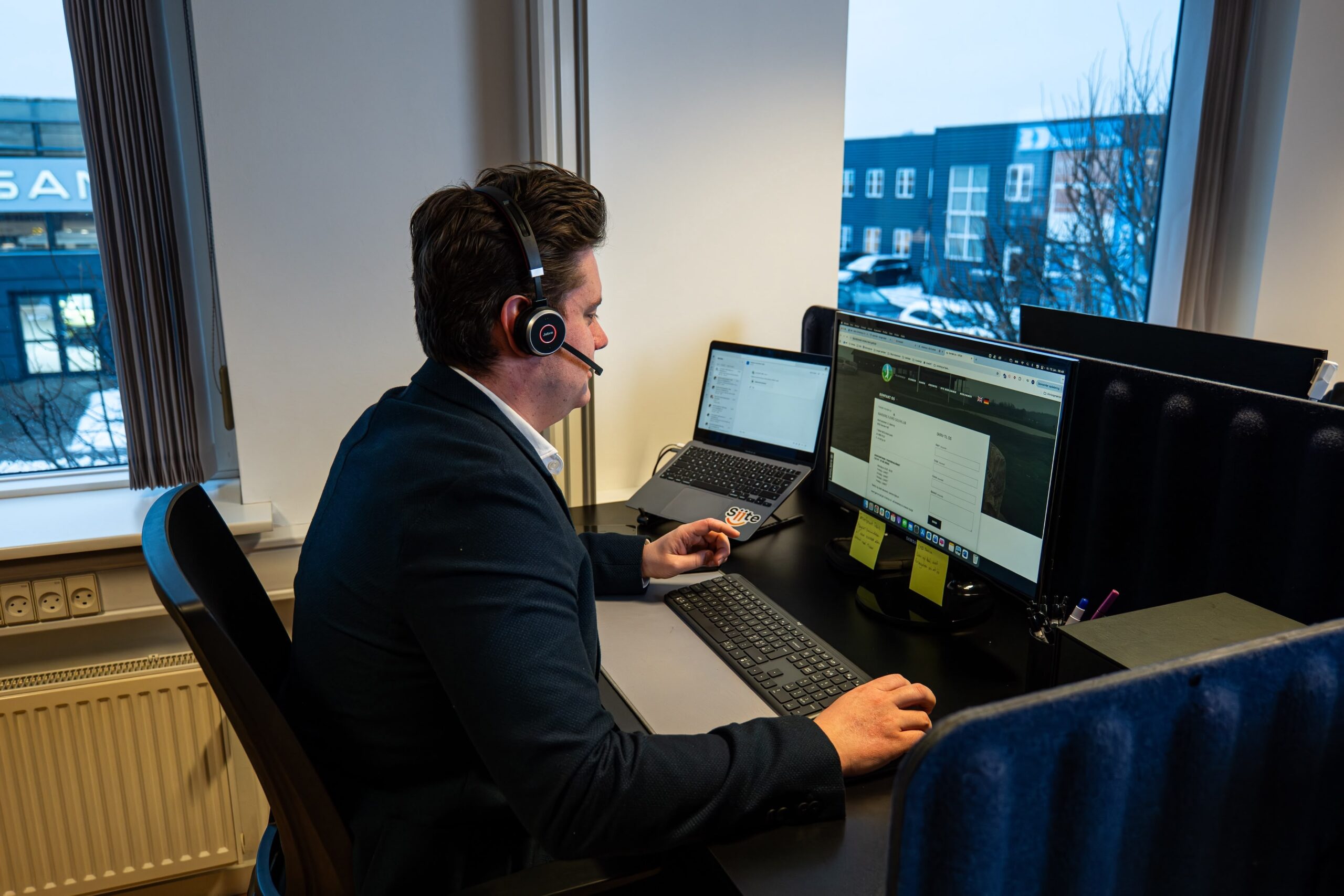 Person arbejder ved computer med headset på kontor.