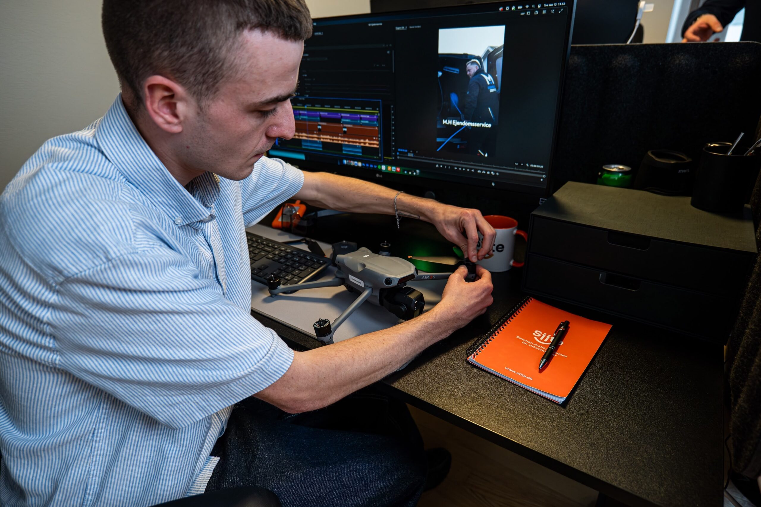 Mand justerer drone ved skrivebord med computer.